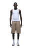 A man stands facing forward against a plain green background, wearing 6PM 6PM+ SHORTS MOCCA CREAM paired with a white sleeveless tank top, white crew socks, and sneakers—perfect for lounging.