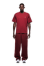 A man faces forward against a plain background, wearing 6PM’s T-SHIRT WINE RED and matching loose pants with small white logos, paired with white sneakers.