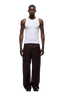 A man faces forward against a white background, wearing a white sleeveless tank top, black shoes, and 6PM WAX COATED DENIM DARK BURGUNDY pants with matte silver details.