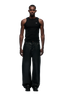 A man faces forward in a fitted black tank top and 6PM WAX COATED DENIM BLACK wide pants with drawstrings and metal buttons, styled with black shoes, set against a plain light gray background.