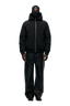 A person stands facing forward in the 6PM EMBOSSED JACKET BLACK, featuring a hidden arm pocket, paired with a black balaclava, loose black pants, and black shoes against a plain light background.