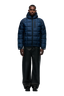 A man faces forward against a plain white background wearing the 6PM LIGHT PUFFER JACKET RECTANGLES MIDNIGHT BLUE, paired with black wide-leg pants and black shoes.