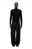 A man faces forward against a plain white background, wearing the 6PM 6PM+ RIBBED LS BLACK top, paired with loose, wide-leg black pants and black shoes.