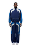 A man stands facing forward, wearing the 6PM EVERYDAY TRACK JACKET SHADOW BLUE with matching track pants and white sneakers, against a plain white background.