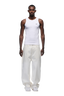 A man stands facing forward against a plain white background, wearing 6PM's WAX COATED DENIM WHITE jeans, a fitted white tank top, and white sneakers.