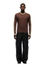 A man stands facing forward in the 6PM GRAFFITI RINGER LS DARK HAZELNUT long-sleeve shirt, paired with loose black pants and black shoes, against a plain white background.