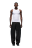 A man faces forward in a fitted white tank and 6PM’s COATED CARPENTER DENIM HASH BROWNIE pants, styled with black shoes, set against a plain white background.