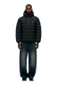 A man faces forward, wearing the 6PM LIGHT WEIGHT PUFFER JACKET BLACK with a hood, wide-leg blue jeans with faded areas, and black shoes, set against a plain light gray background.