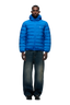 A man faces forward in a 6PM LIGHT WEIGHT PUFFER JACKET PRINCESS BLUE with a hood, wide-leg blue jeans, and black shoes against a plain white background.