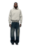 A man faces forward wearing the 6PM COLLEGE LETTER HOODIE in smoke grey and oversized dark blue faded jeans with black shoes, set against a plain white background.