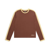 The GRAFFITI RINGER LS DARK HAZELNUT by 6PM is a long-sleeve brown shirt with light yellow trim on the collar, cuffs, and sleeves, plus a small embroidered logo near the bottom left hem.