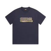 The CLEAN EDGE WAVE T-SHIRT MIDNIGHT BLUE by 6PM is a navy short-sleeve shirt with bold yellow “SIXPM” lettering and a stylized underline on the chest, displayed flat against a white background.