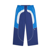 The 6PM EVERYDAY TRACK PANTS SHADOW BLUE feature blue and white wide-leg panels, white piping, an elastic waistband, and side pockets, shown on a white background.