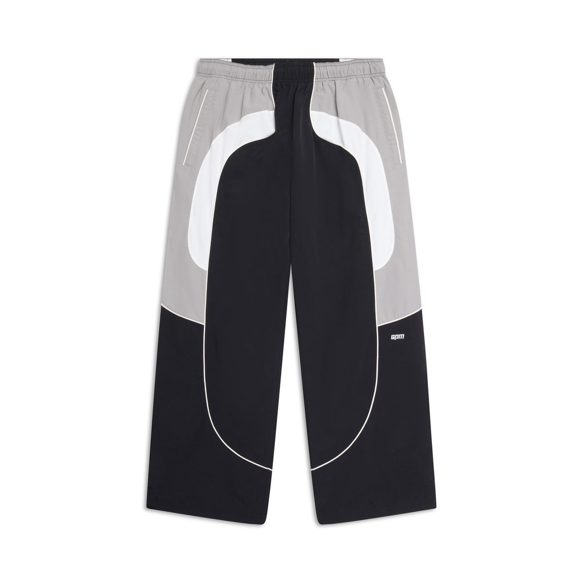 The 6PM EVERYDAY TRACK PANTS BLACK are wide-leg pants with a drawstring waist, bold curved colorblock in black, white, and gray, side pockets, and a small white logo on one leg.