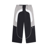 The 6PM EVERYDAY TRACK PANTS BLACK are wide-leg pants with a drawstring waist, bold curved colorblock in black, white, and gray, side pockets, and a small white logo on one leg.