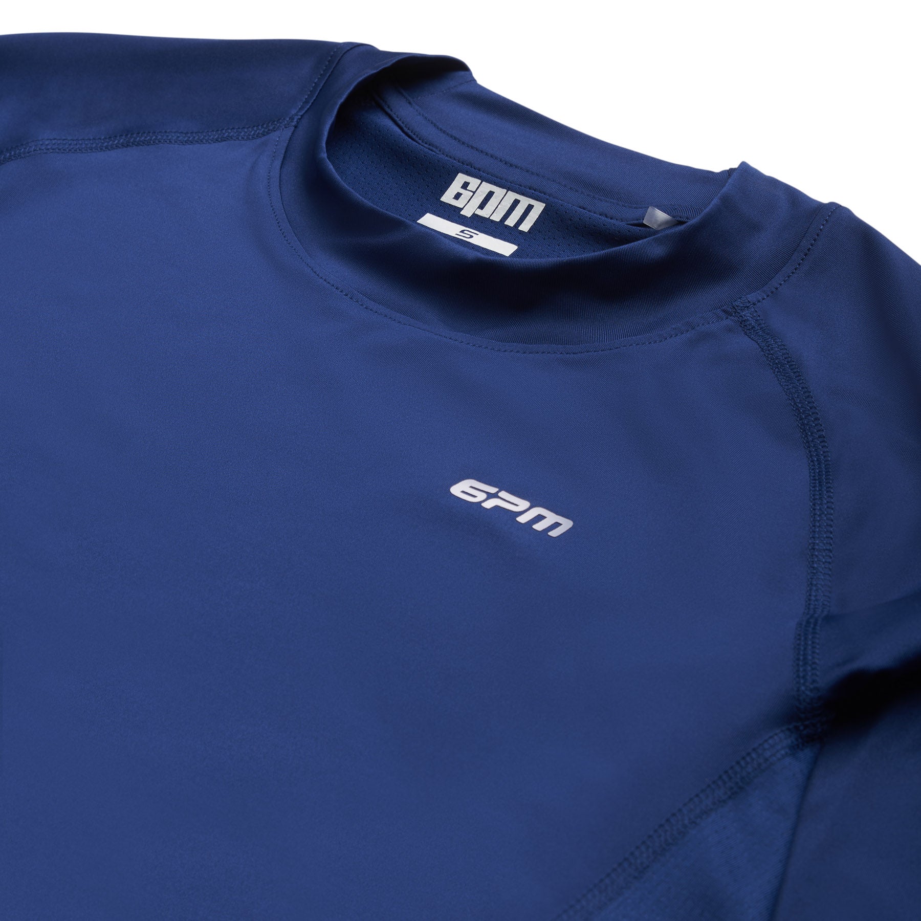 A close-up of the 6PM SPORTS LONGSLEEVE DEEP SEA BLUE by 6PM, showcasing the white 6PM logo on the chest and collar. This athletic shirt features a crew neckline and smooth, stretchy fabric.