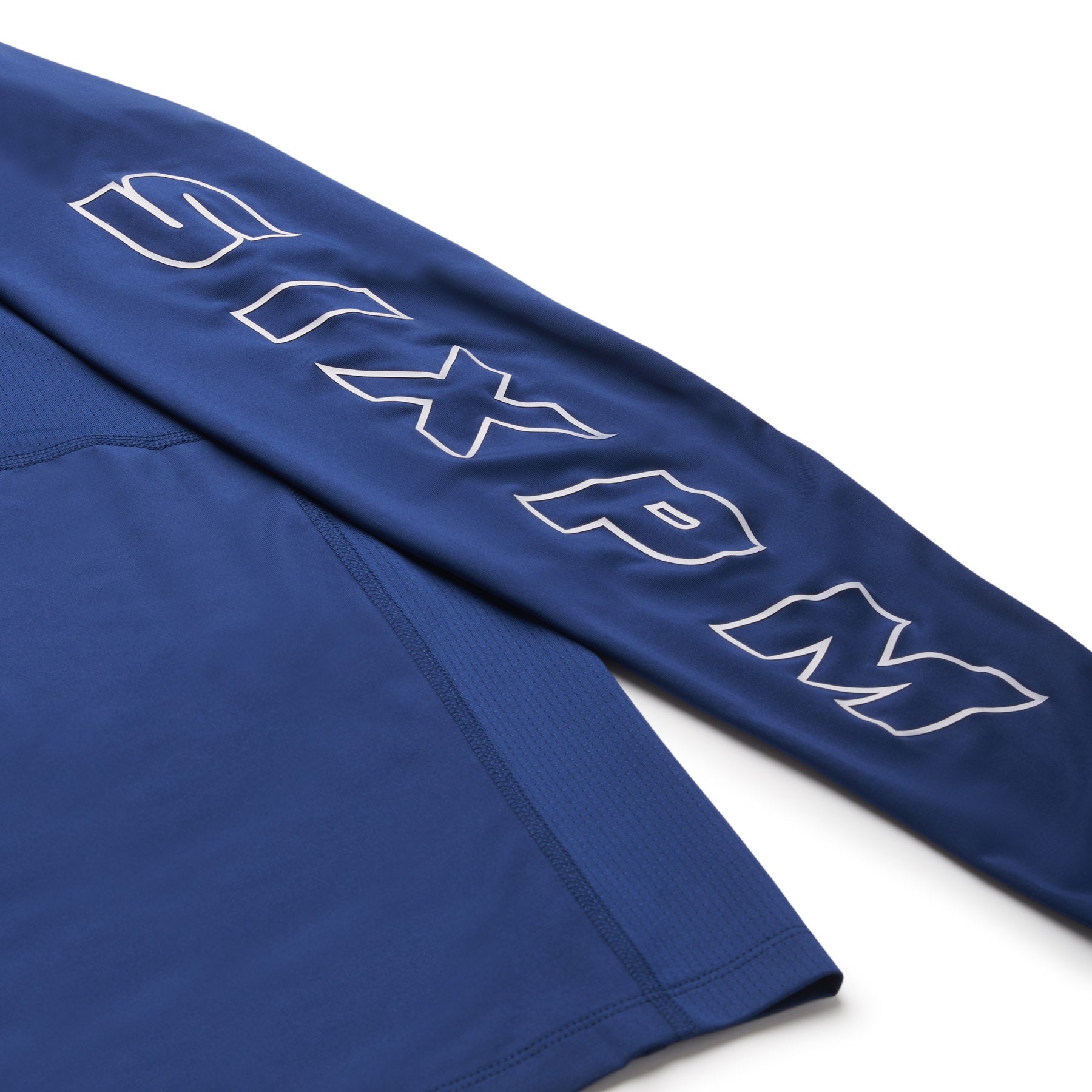 A close-up of the 6PM SPORTS LONGSLEEVE DEEP SEA BLUE by 6PM shows smooth, slightly stretchy fabric and large outlined silver "SIXPM" lettering along the sleeve.