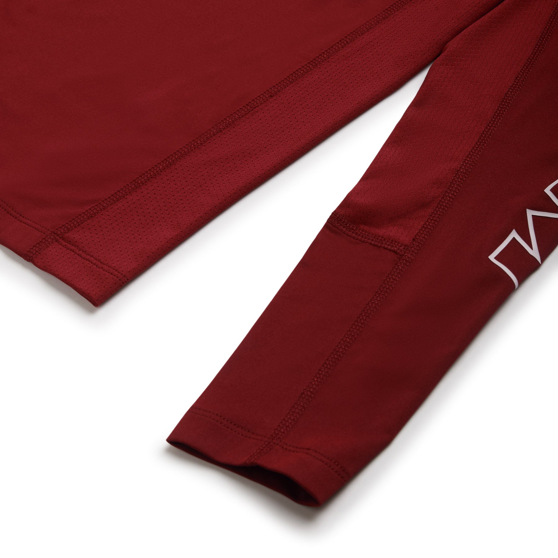 Close-up of the 6PM SPORTS LONGSLEEVE WINE RED by 6PM, highlighting stitching details and part of the white printed sleeve logo. The lightweight, breathable fabric is visible.