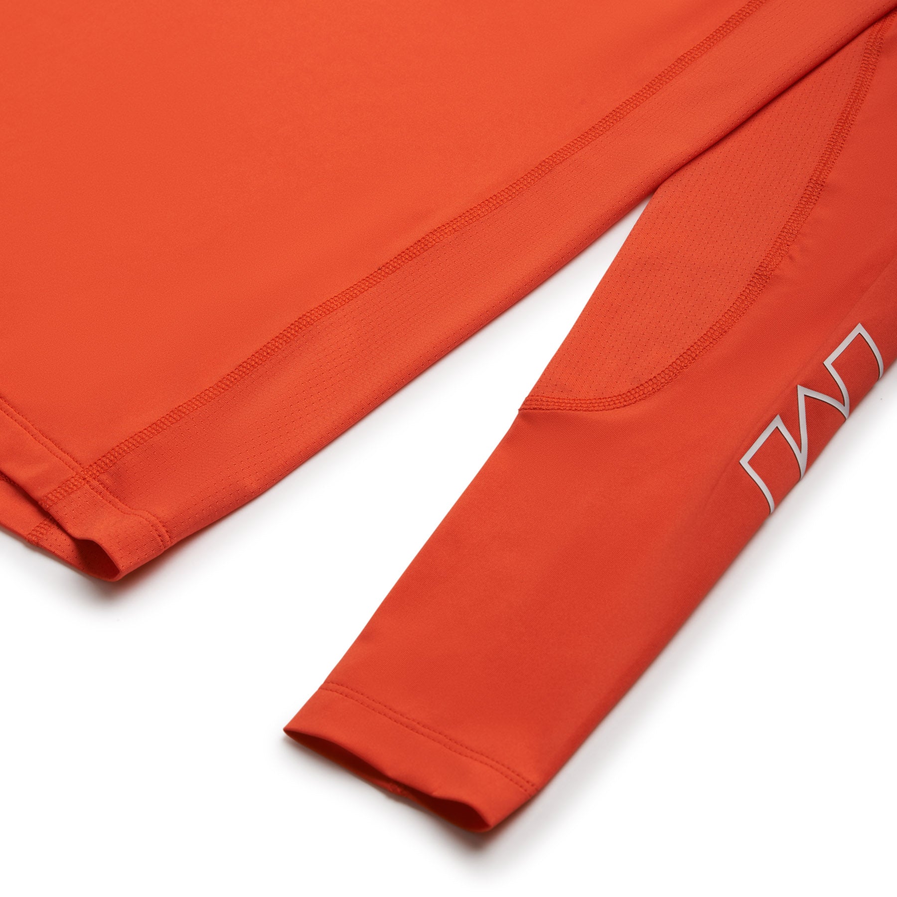 Close-up of the 6PM SPORTS LONGSLEEVE SUNSTONE RED shirt by 6PM, featuring orange fabric and a white geometric design near the sleeve cuff, shown on a white background.
