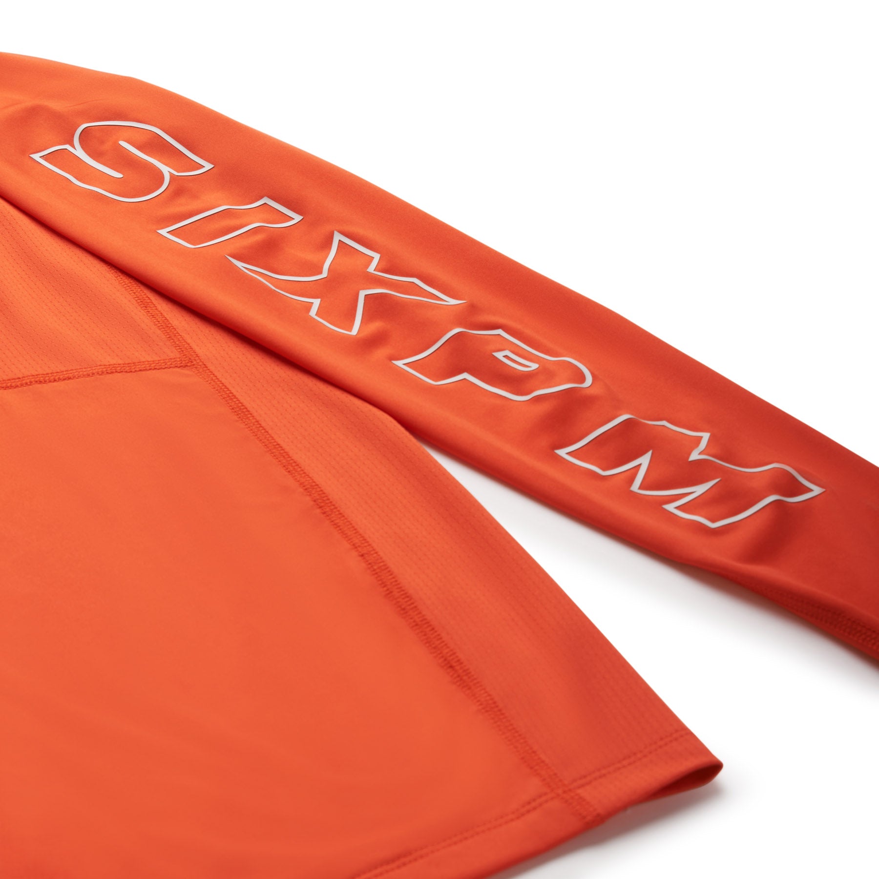 The 6PM SPORTS LONGSLEEVE SUNSTONE RED by 6PM is an orange long-sleeve shirt shown on a white background, with “SIXPM” in bold, white outlined letters along the sleeve.