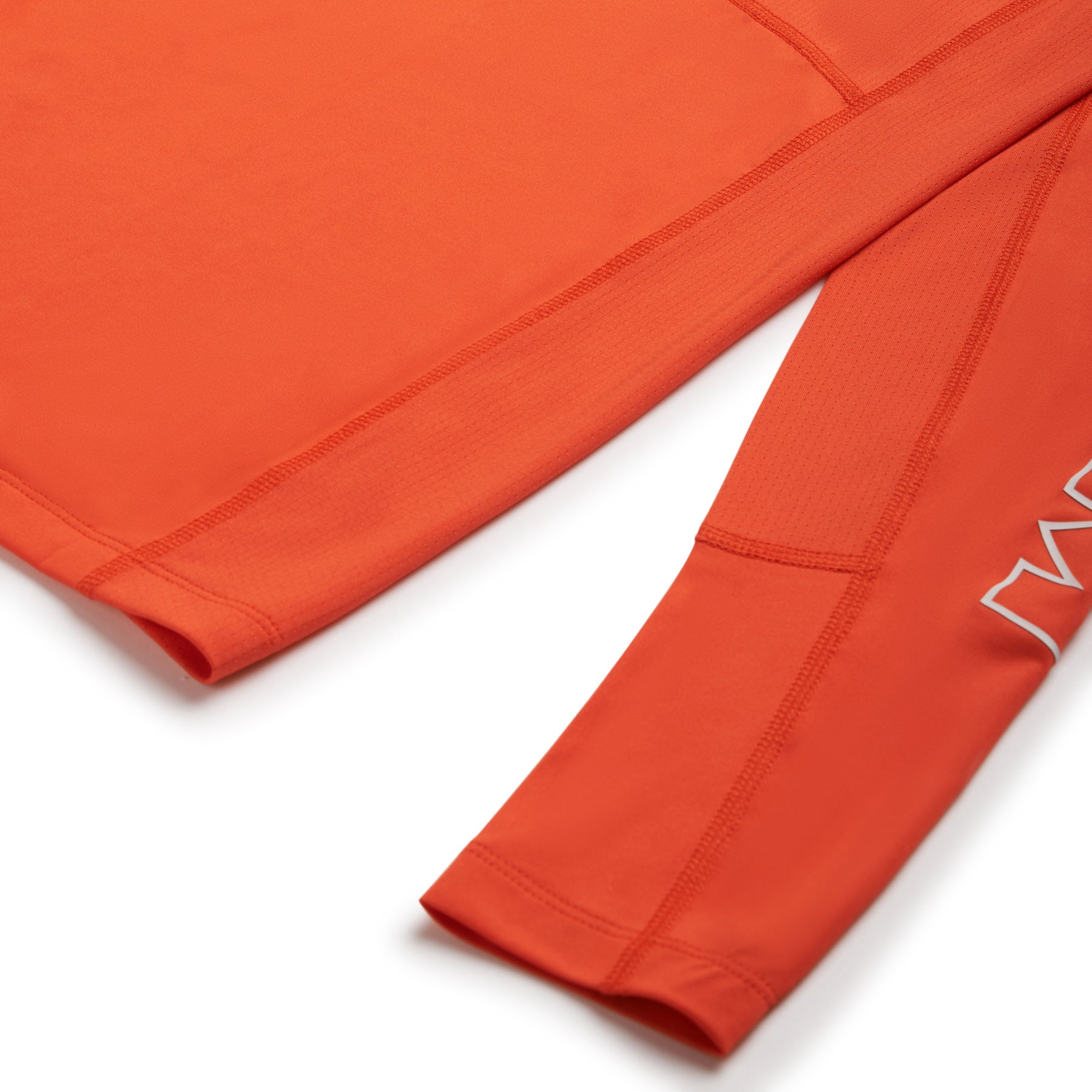 Close-up of the 6PM SPORTS LONGSLEEVE SUNSTONE RED by 6PM, highlighting the orange sleeve with a visible seam and partial white logo. The smooth, textured fabric is showcased along the sleeve and body.