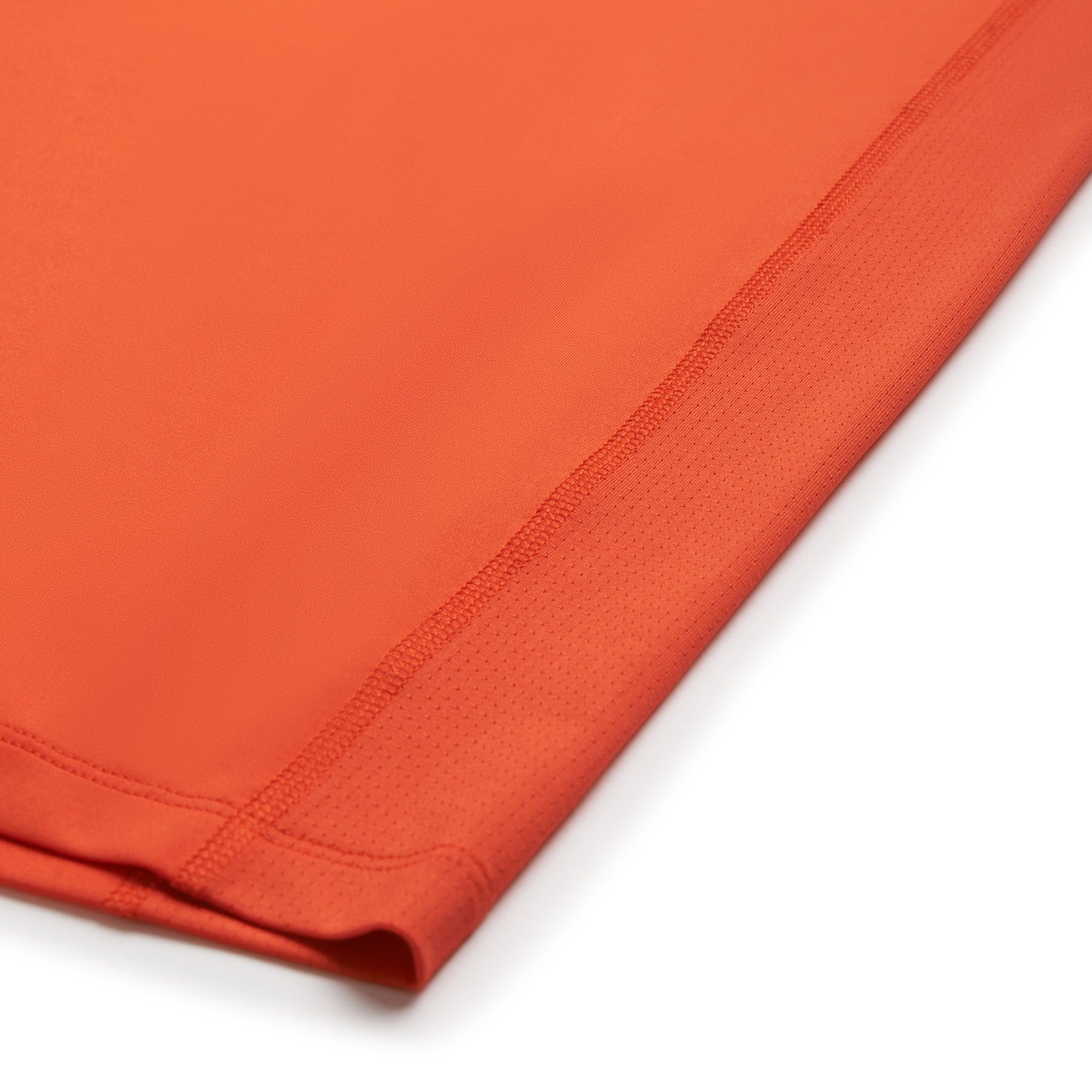 Close-up of the hem on the 6PM SPORTS T-SHIRT SUNSTONE RED by 6PM, featuring smooth, stretchy fabric with subtle mesh detailing at the edge and neat stitching.