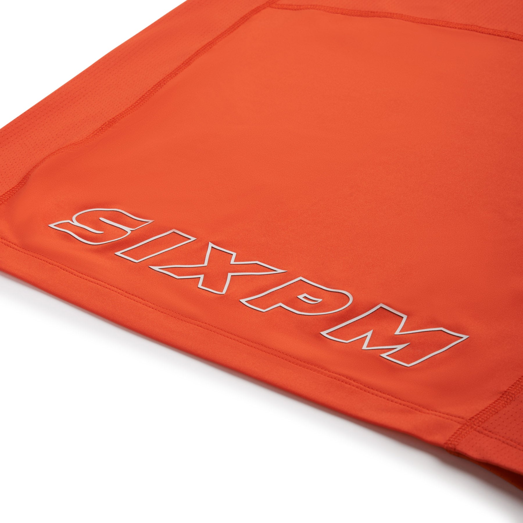 Close-up of the 6PM SPORTS T-SHIRT SUNSTONE RED, featuring bold, outlined white "6PM" branding on sporty, breathable orange fabric.