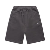 6PM+ SHORTS ANTHRACITE by 6PM: Dark gray athletic shorts with relaxed fit, elastic waistband, side pockets, and a small white 6PM logo on the left leg. Displayed flat on a white background.