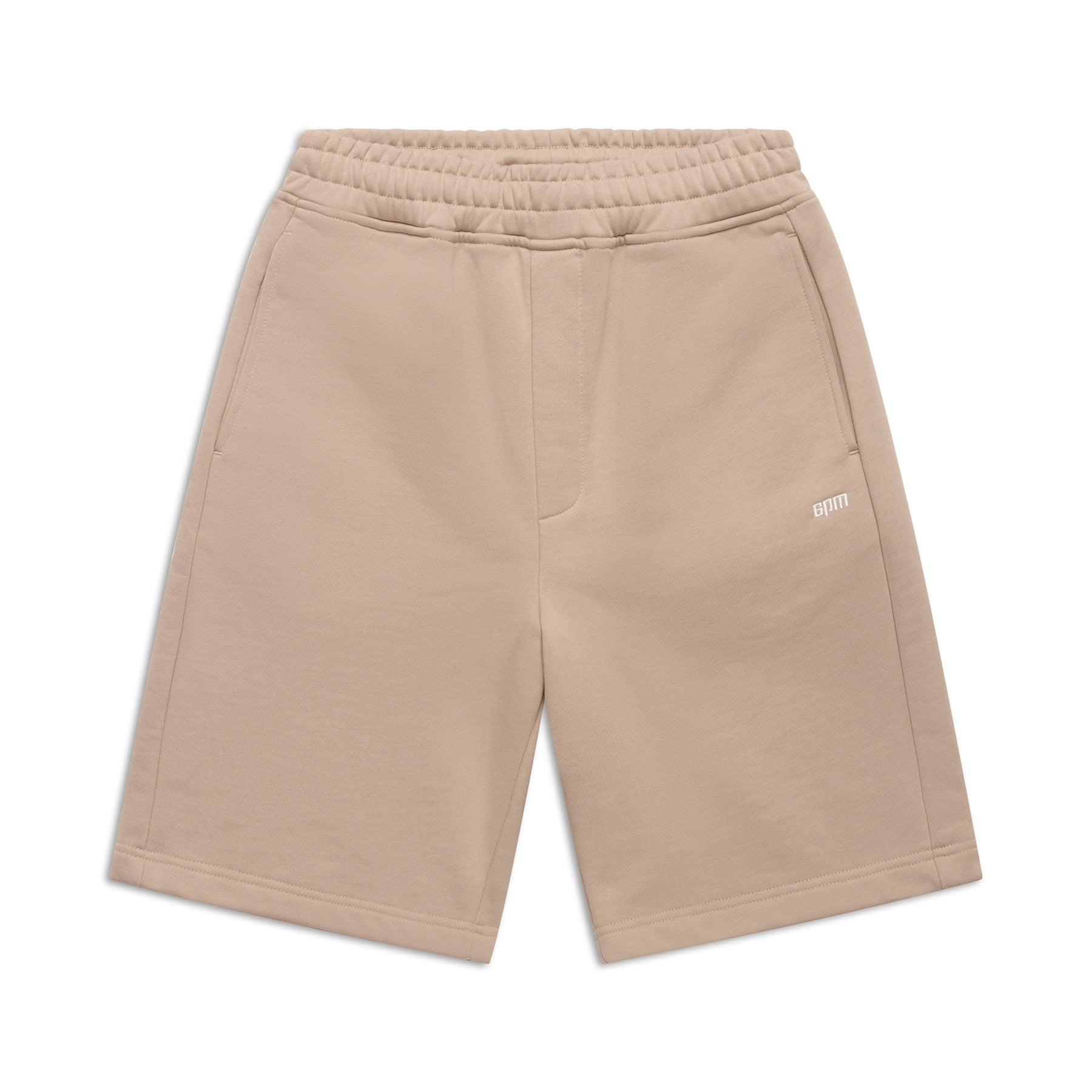 The 6PM+ SHORTS MOCCA CREAM by 6PM are beige, knee-length with a relaxed fit, elastic waistband, side pockets, and a small white embroidered logo on the left thigh—ideal for lounging. Shown flat on a white background.