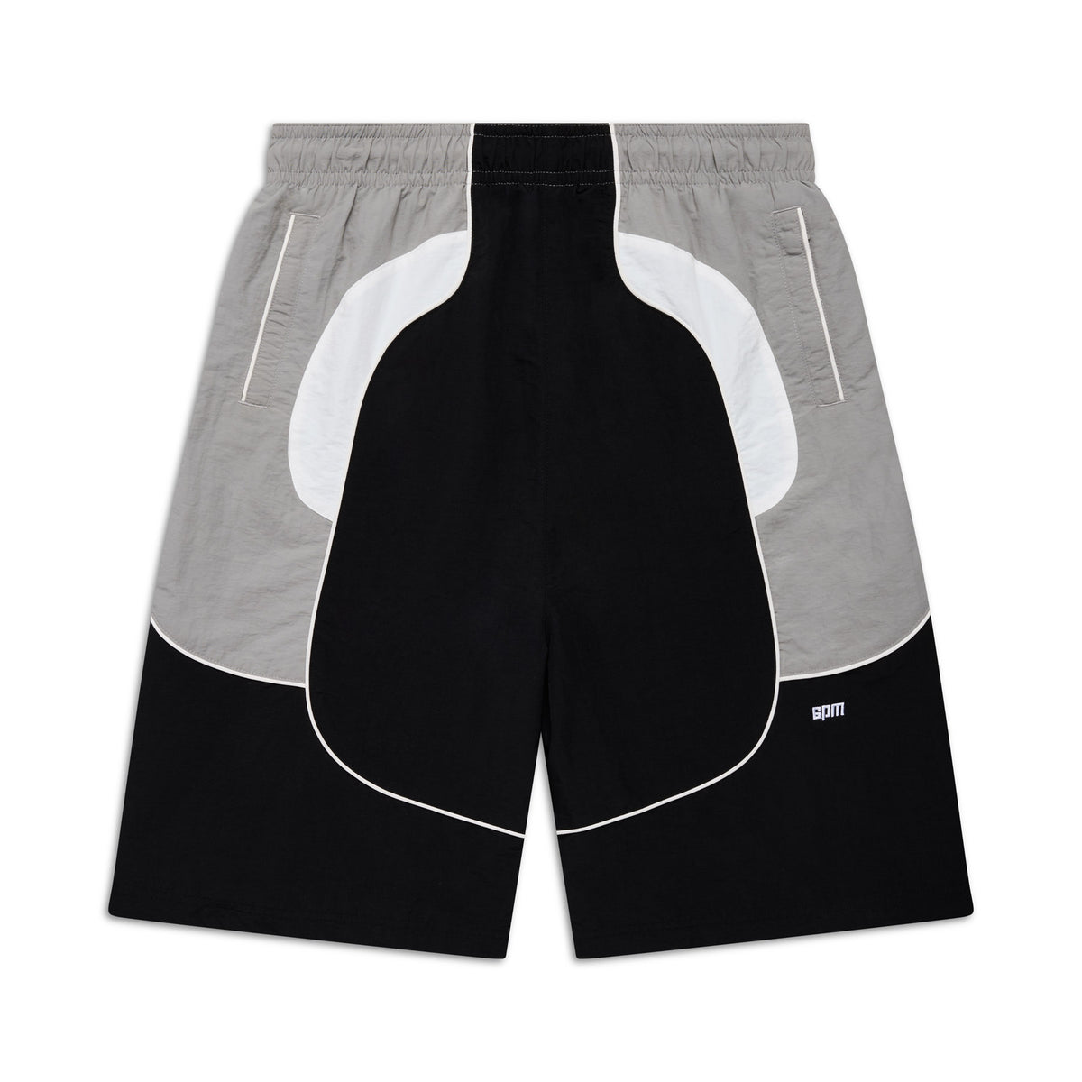 The BAGGY WARM UP SHORTS BLACK by 6PM feature black, white, and gray color-blocked panels with curved lines, an elastic waistband, zippered side pockets, and a small 6PM logo on the lower right leg. Shorts are shown laid flat on a white background.