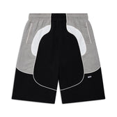 The BAGGY WARM UP SHORTS BLACK by 6PM feature black, white, and gray color-blocked panels with curved lines, an elastic waistband, zippered side pockets, and a small 6PM logo on the lower right leg. Shorts are shown laid flat on a white background.
