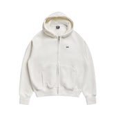 The 6PM ZIP HOODIE COCONUT WHITE features a clean, structured look with front pockets and a small black embroidered logo on the left chest, making it perfect for everyday wear.