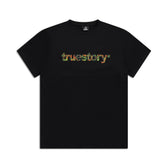The 6PM TRUE STORY T-SHIRT BLACK features truestory in a vibrant floral print across the chest, shown on a white background.