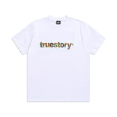 The 6PM TRUE STORY T-SHIRT WHITE features “truestory” in colorful, floral-inspired lettering across the chest.