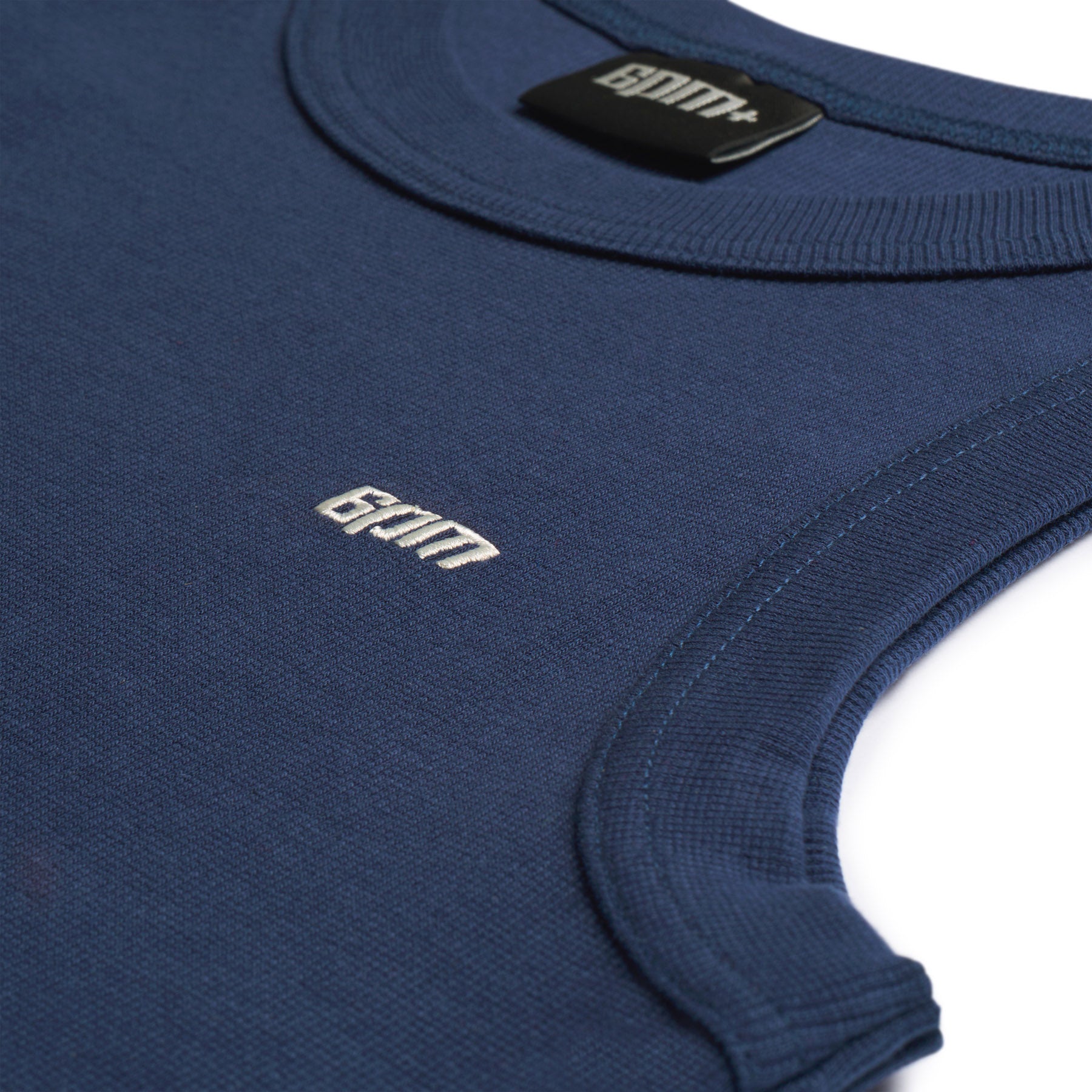 Close-up of the 6PM TANK TOP NAVY, a sleeveless navy blue ribbed tank featuring “GYM” embroidered in white on the chest and a black inner collar label with the same text.