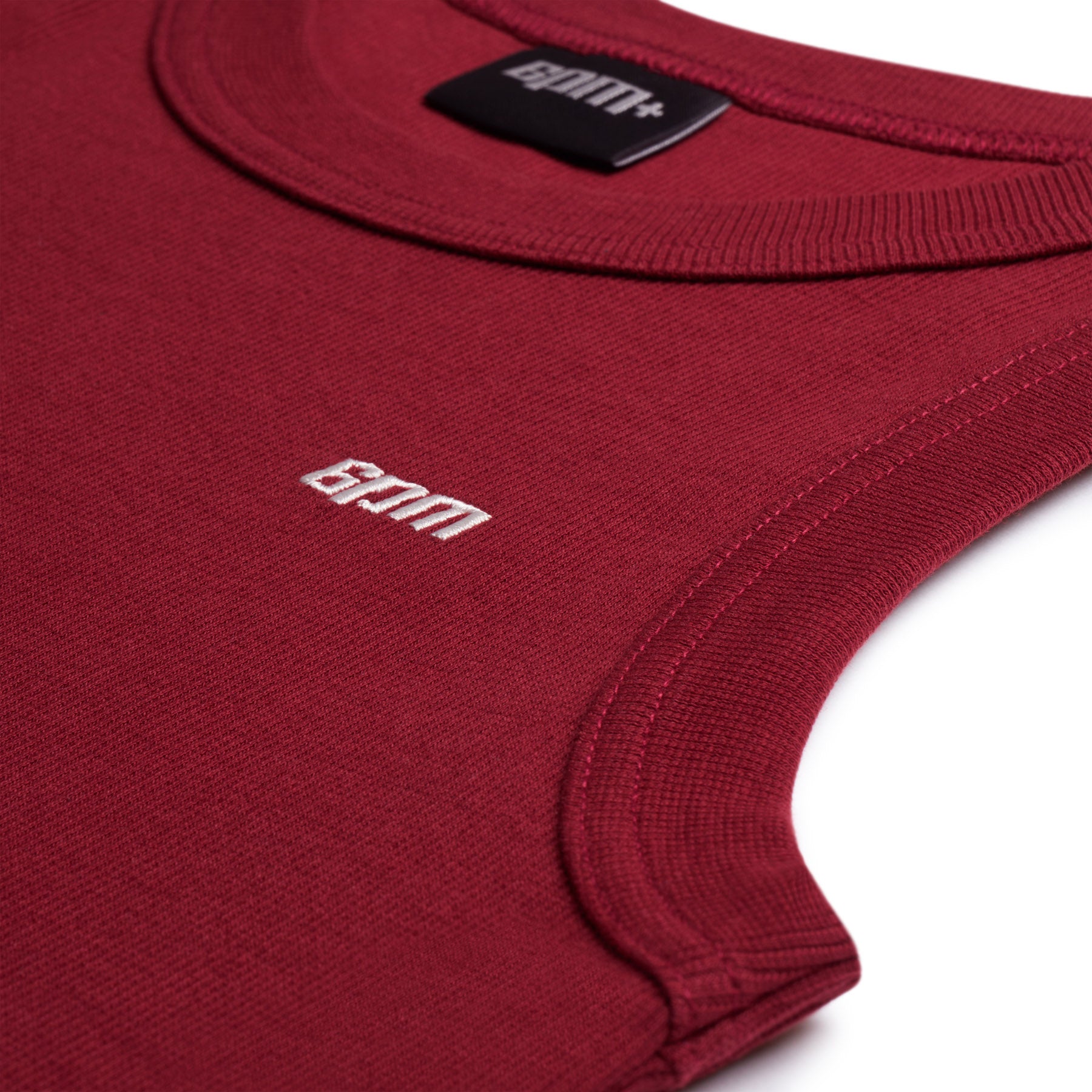 Close-up of the 6PM TANK TOP WINE RED, a sleeveless top with ribbed edges and a small white Gym logo embroidered on the chest. The neckline features a visible clothing label.