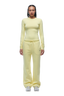 A person stands facing forward in a 6PM WMNS LONGSLEEVE BUTTERCREAM top and matching loose yellow sweatpants with drawstrings, paired with white sneakers. The background is plain white.