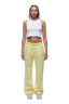 A woman with braided hair and a neutral expression faces forward, wearing the 6PM WMNS OPEN LEG BUTTERCREAM sweatpants, a white cropped tank top, and white sneakers.