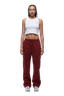 A woman with braided hair wears the 6PM WMNS OPEN LEG WINE RED sweatpants, styled with a white crop top and sneakers. She stands facing forward against a plain white background.