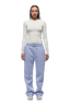 A person with braided hair and a neutral expression stands against a white background wearing the 6PM WMNS LONGSLEEVE OFF-WHITE shirt, light blue drawstring sweatpants, and silver sneakers.