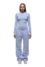 A person with braided hair stands facing forward, wearing the 6PM WMNS LONGSLEEVE SOFT VIOLET top and matching sweatpants with white sneakers.