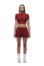 A woman with braided hair wears the 6PM WMNS CROPPED T-SHIRT WINE RED, maroon shorts, white socks, and white sneakers, standing facing forward with a neutral expression against a white background.