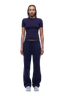 A woman with braided hair faces forward, wearing the 6PM WMNS T-SHIRT ORBIT BLUE, matching sweatpants, and white sneakers against a plain white background.