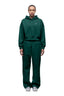 A person faces forward against a plain white background, wearing the 6PM WMNS CROPPED HOODIE EVERGREEN with matching wide-leg sweatpants and white sneakers.